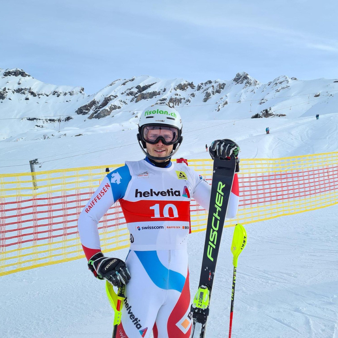 Noel von Grünigen mit Skiern in der Hand vor einem Bergmassiv
