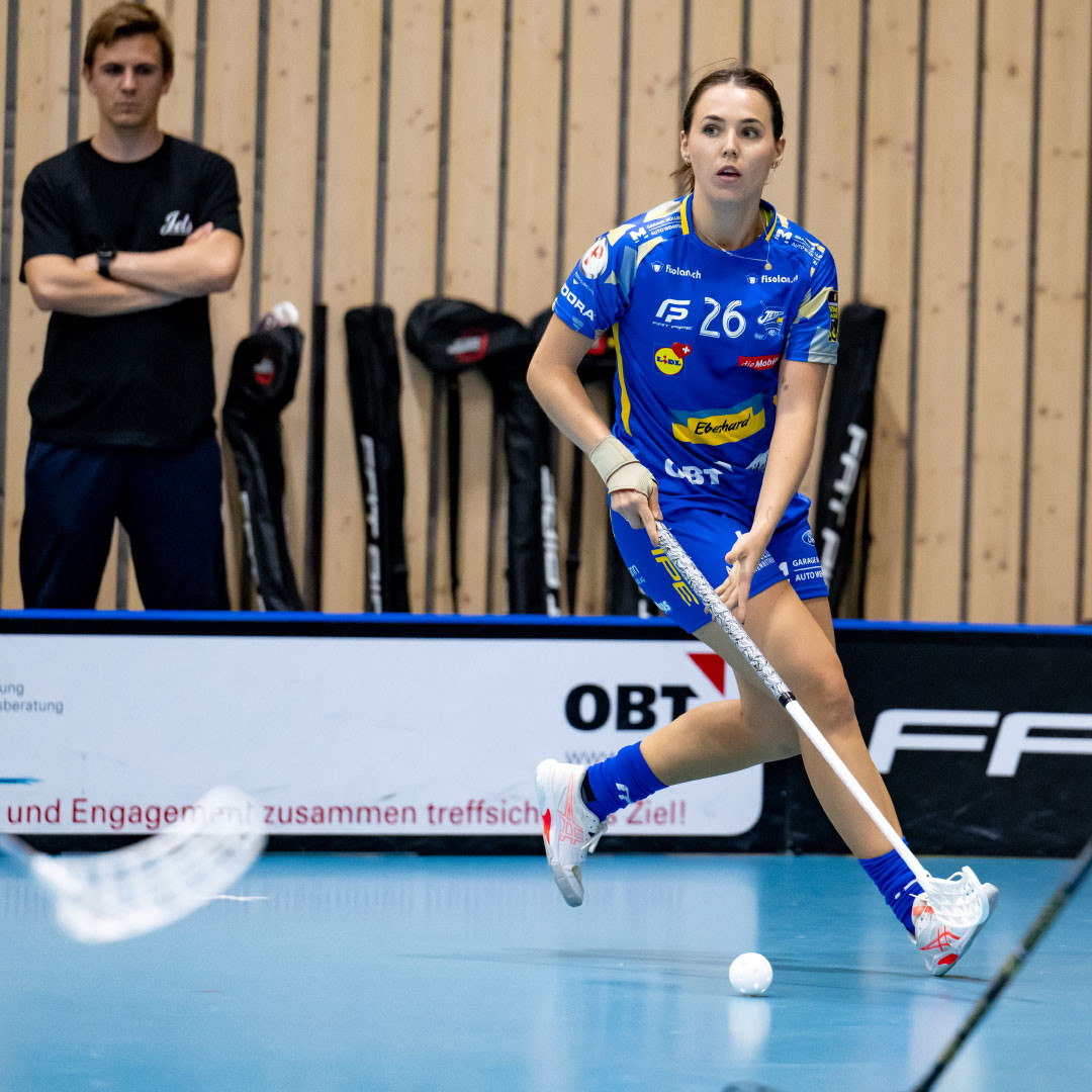 Céline Stettler en maillot bleu sur le ballon avec un bâton de floorball