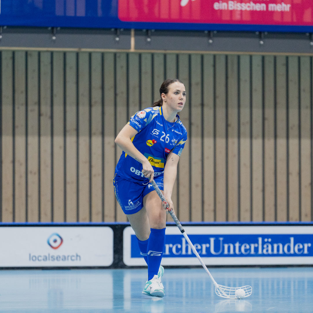 Céline Stettler en maillot bleu avec le ballon de floorball et le bâton sur le terrain en courant