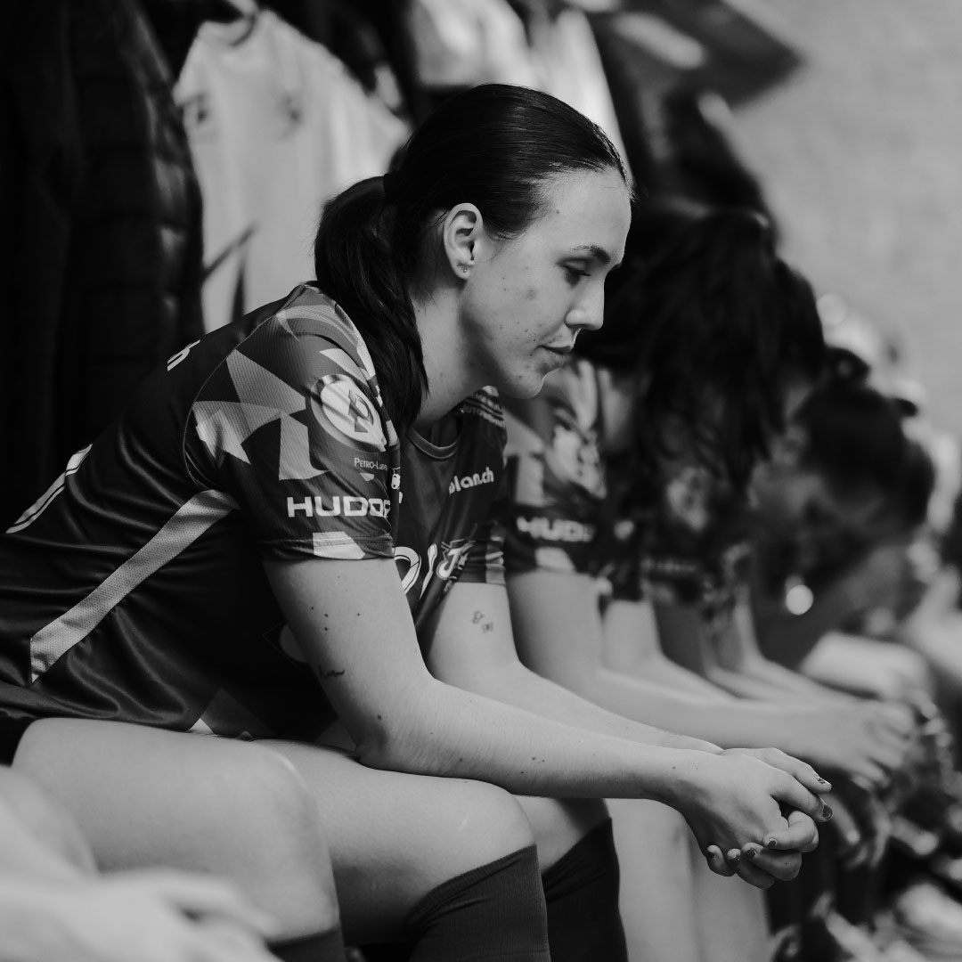 Photo en noir et blanc de Céline Stettler assise sur un banc à côté de coéquipières, les yeux baissés