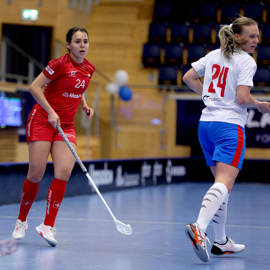 Céline Stettler en maillot rouge se concentre sur le terrain de floorball avec un adversaire devant elle