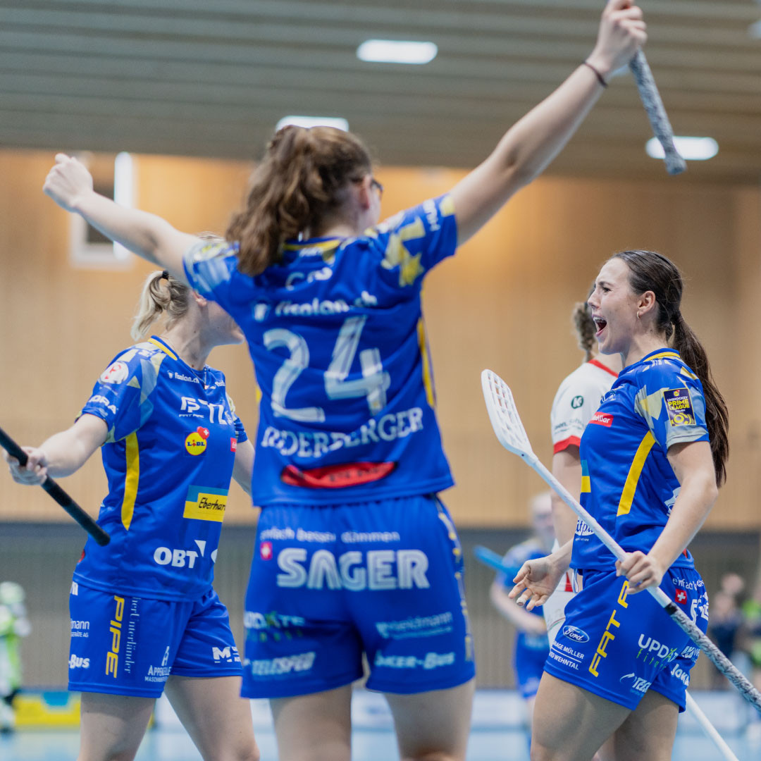 Céline Stettler applaudit avec deux coéquipiers en maillot bleu avec des bâtons de floorball dans leurs mains