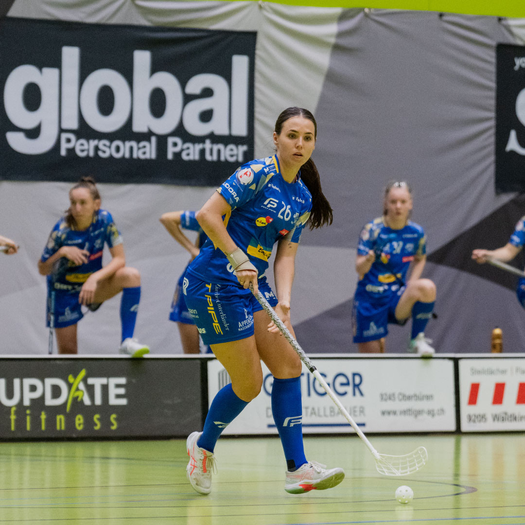 Céline Stettler en maillot bleu avec le ballon de floorball et le bâton sur le terrain en courant