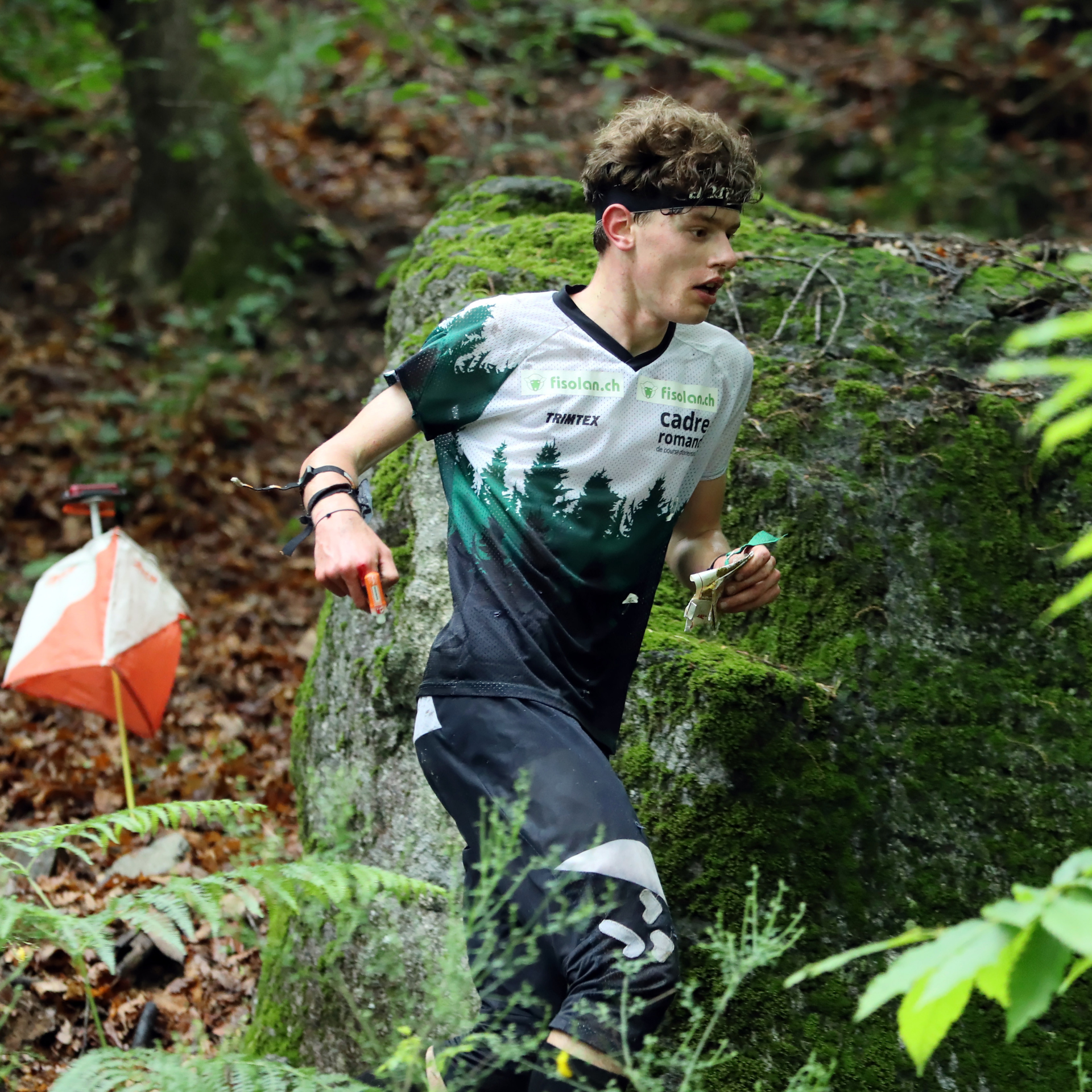 Matthieu Bührer en tenue de sport, courant dans la forêt à côté d'un poste de course d'orientation.