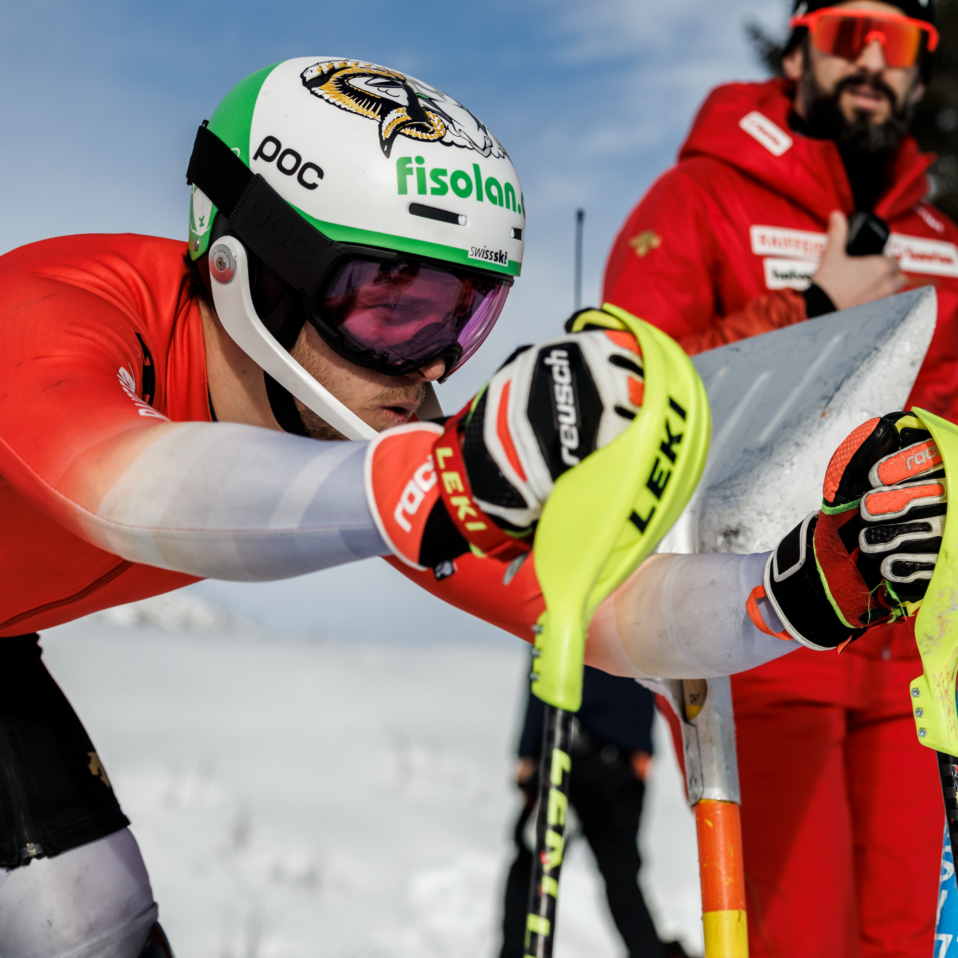 Noel von Grünigen mit weiss grünem Helm in Sunrise Skidress auf Skistöcken aufgestützt mit Blick nach vorne