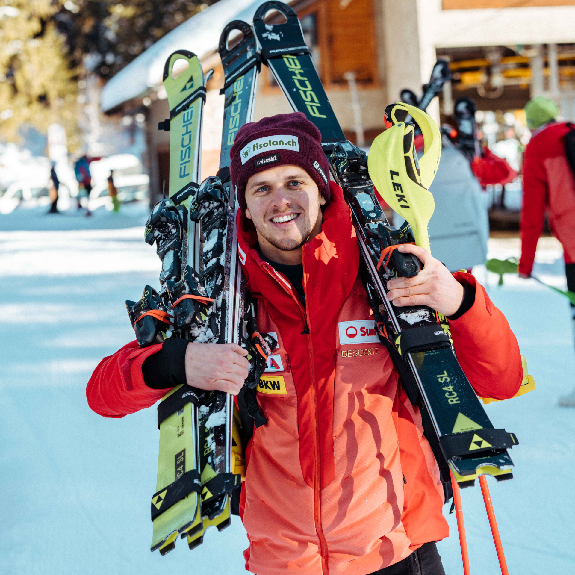 Noel von Grünigen avec une veste rouge et un bonnet noir avec des skis sur l'épaule