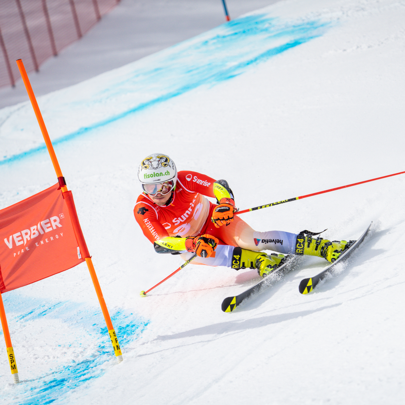 Noel von Grünigen passe en tenue de ski rouge, accroupi devant un petit drapeau rouge