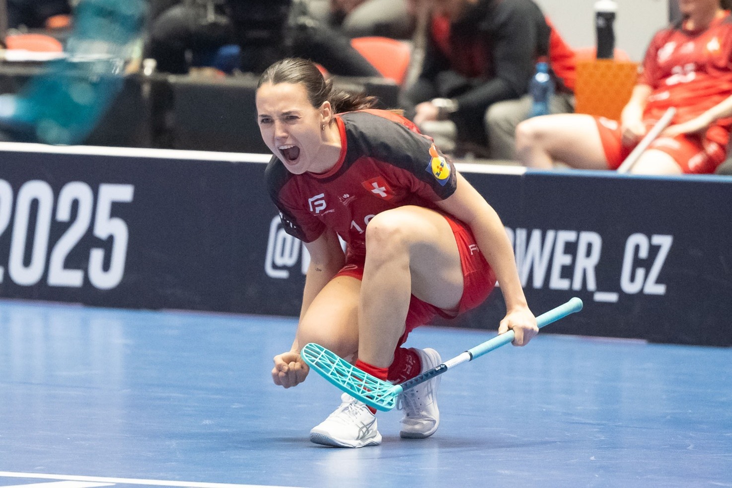 Céline Stettler, crosse d'unihockey à la main, accroupie sur le terrain, le bras tendu, dans une pose de victoire, en train de célébrer